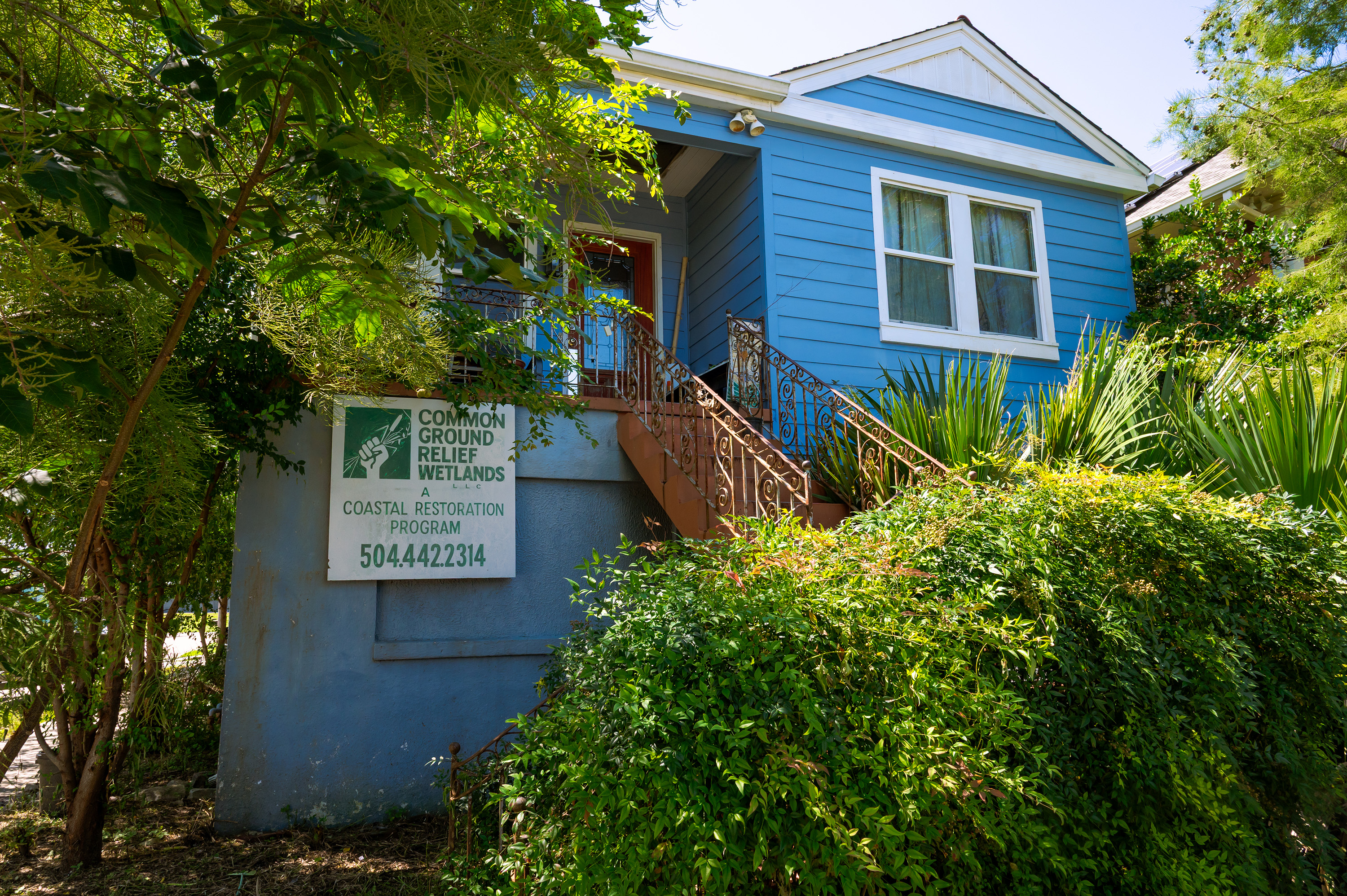 A blue building with a sign that reads, "Common Ground Relief Wetlands," surrounded by green trees and bushes.