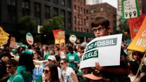 A boy with brown hair holds a sign that says "end fossil fuels"