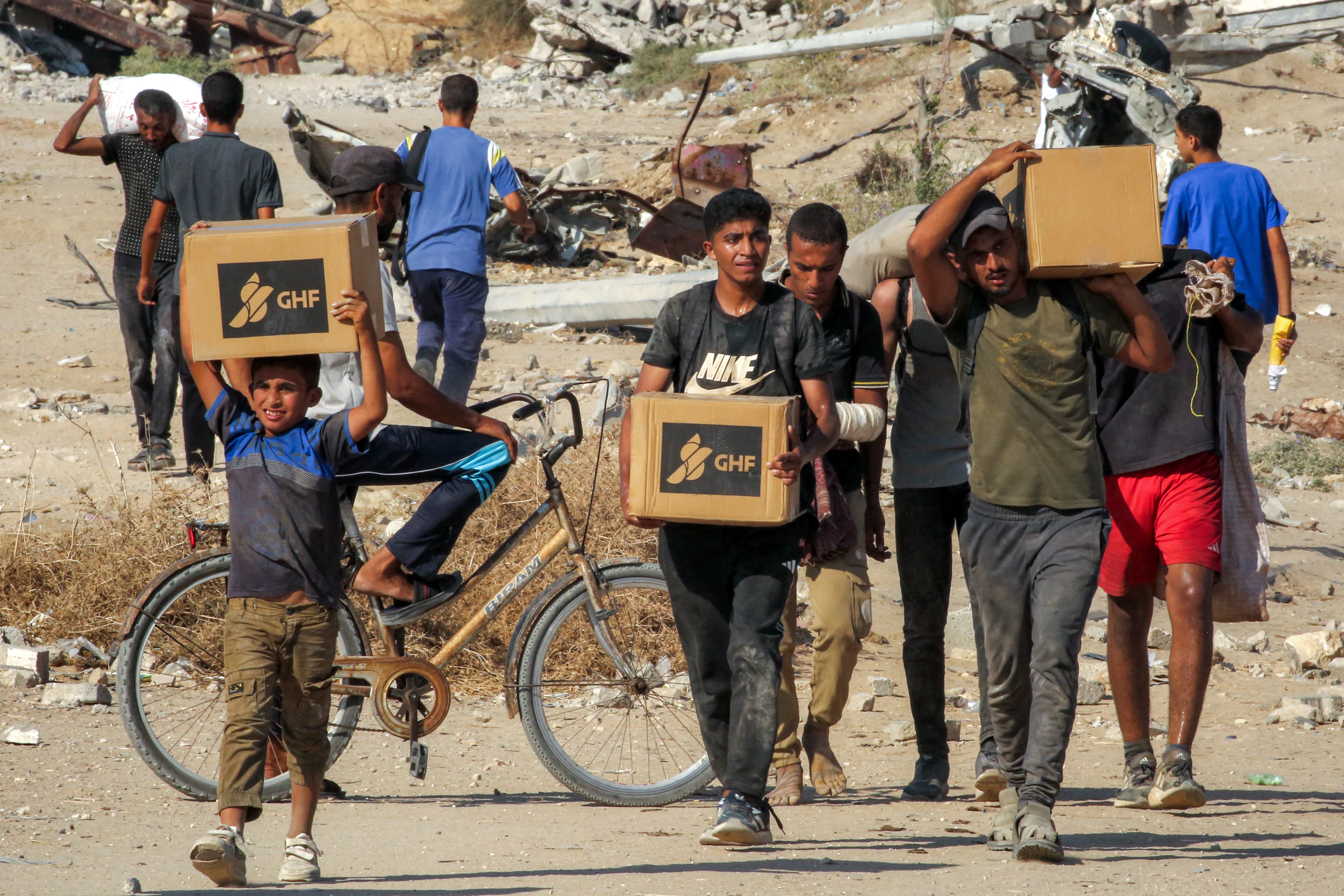 Boys and young men walk while carrying cardboard boxes with GHF logos on the side. 