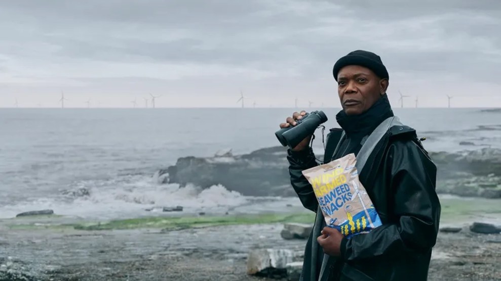 A Black man holding a bag of chips by the seaside.