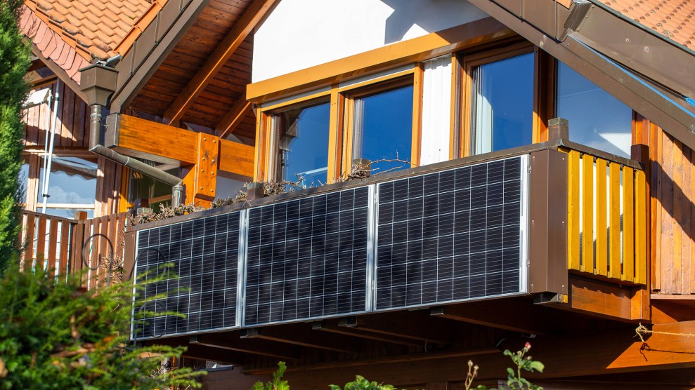 A solar panel affixed to a balcony on a white and brown house.