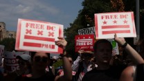 Two people hold signs with the DC flag reading "FREE DC"