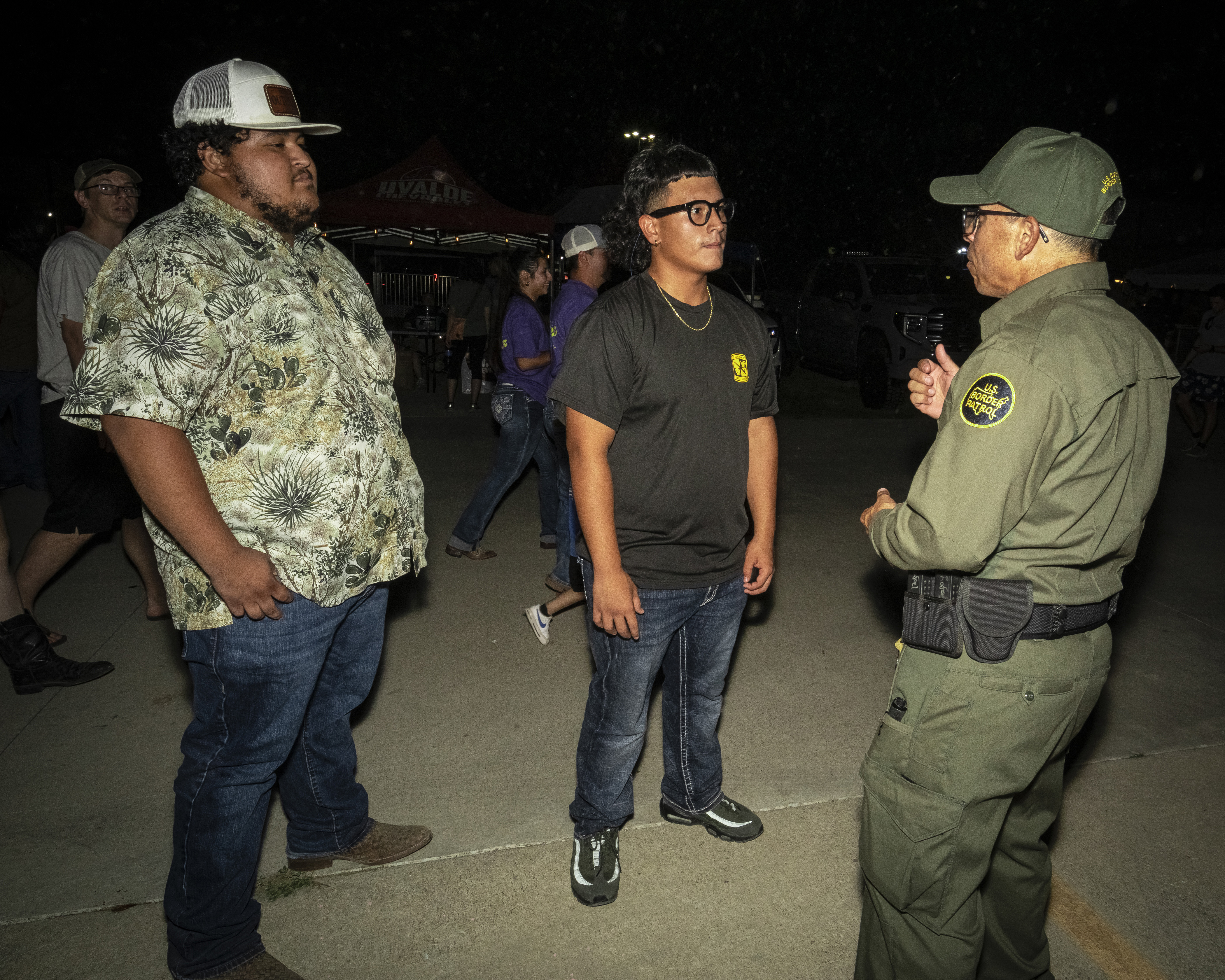A Border Patrol agent in uniform talks to two young men.