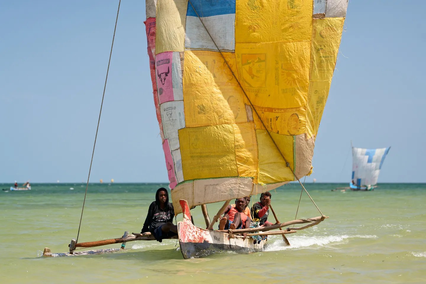 Fishermen on a small sailboat with a yellow sail.