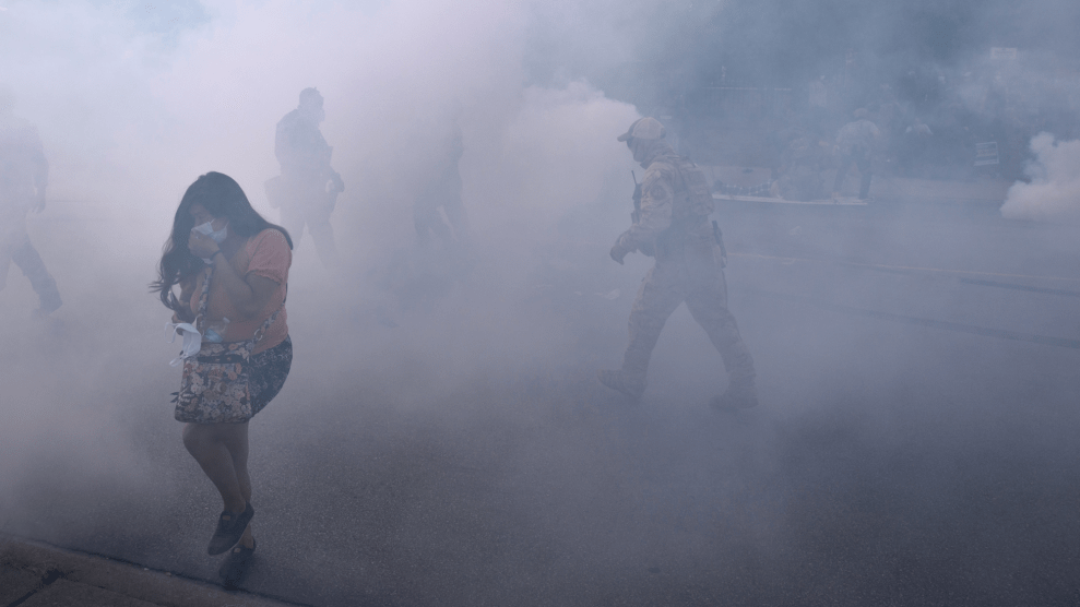 A woman in a mask walks through a cloud of tear gas.
