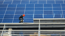 A man dressed in black wearing a red hard hat crouches as he lowers one of dozens of panels into place.