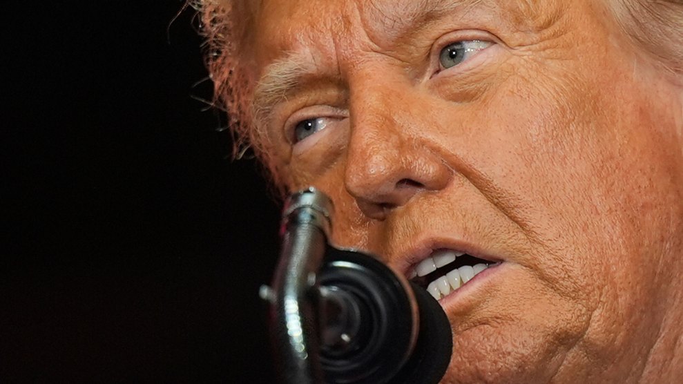 tight shot of Trump's orange-caked face speaking into a microphone against a black background