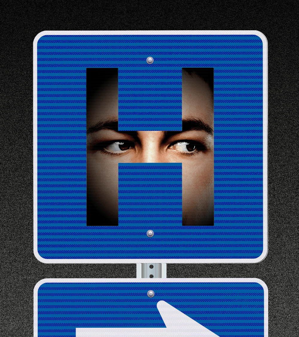 A hospital road sign in which there is a face hidden in the shadows behind the shape of the H. The eyes of the face appear to be staring intently to our right.