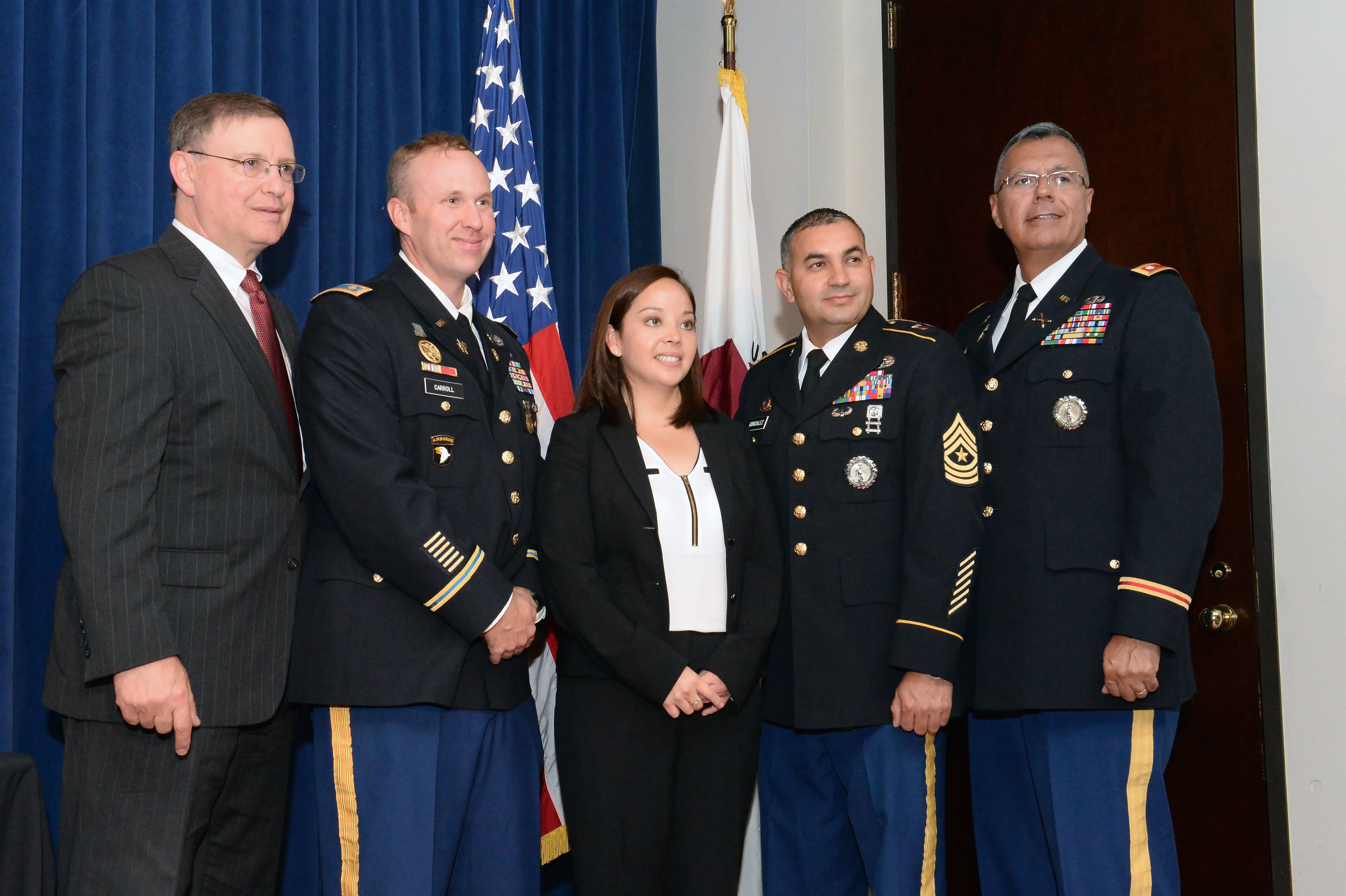 A woman in a pants suit flanked by men in military uniforms.