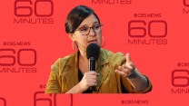 Bari Weiss, a bespectacled woman, speaks into a microphone; behind her is a repeating pattern of the CBS 60 Minutes logo.