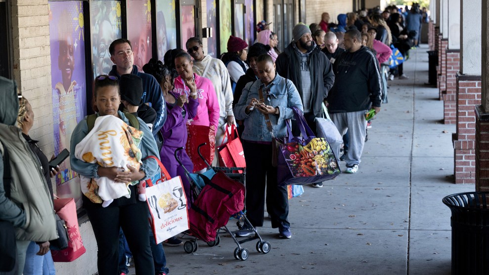 A long line and diverse crowd of people stand waiting outside of a food bank.