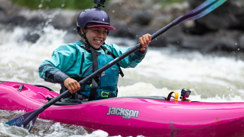 A person in a pink kayak smiles while paddling through a river.