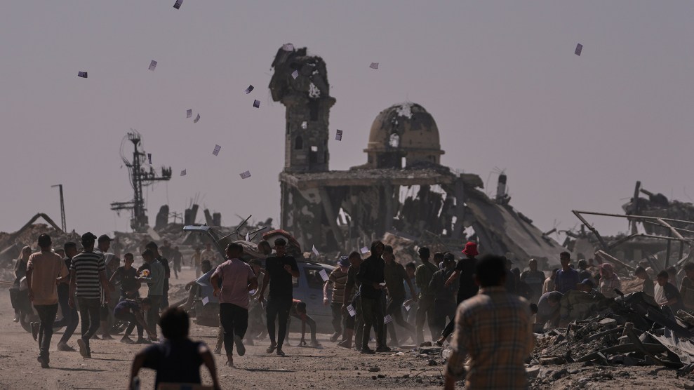 Palestinians walk through a destroyed city. Leaflets drift through a hazy sky.