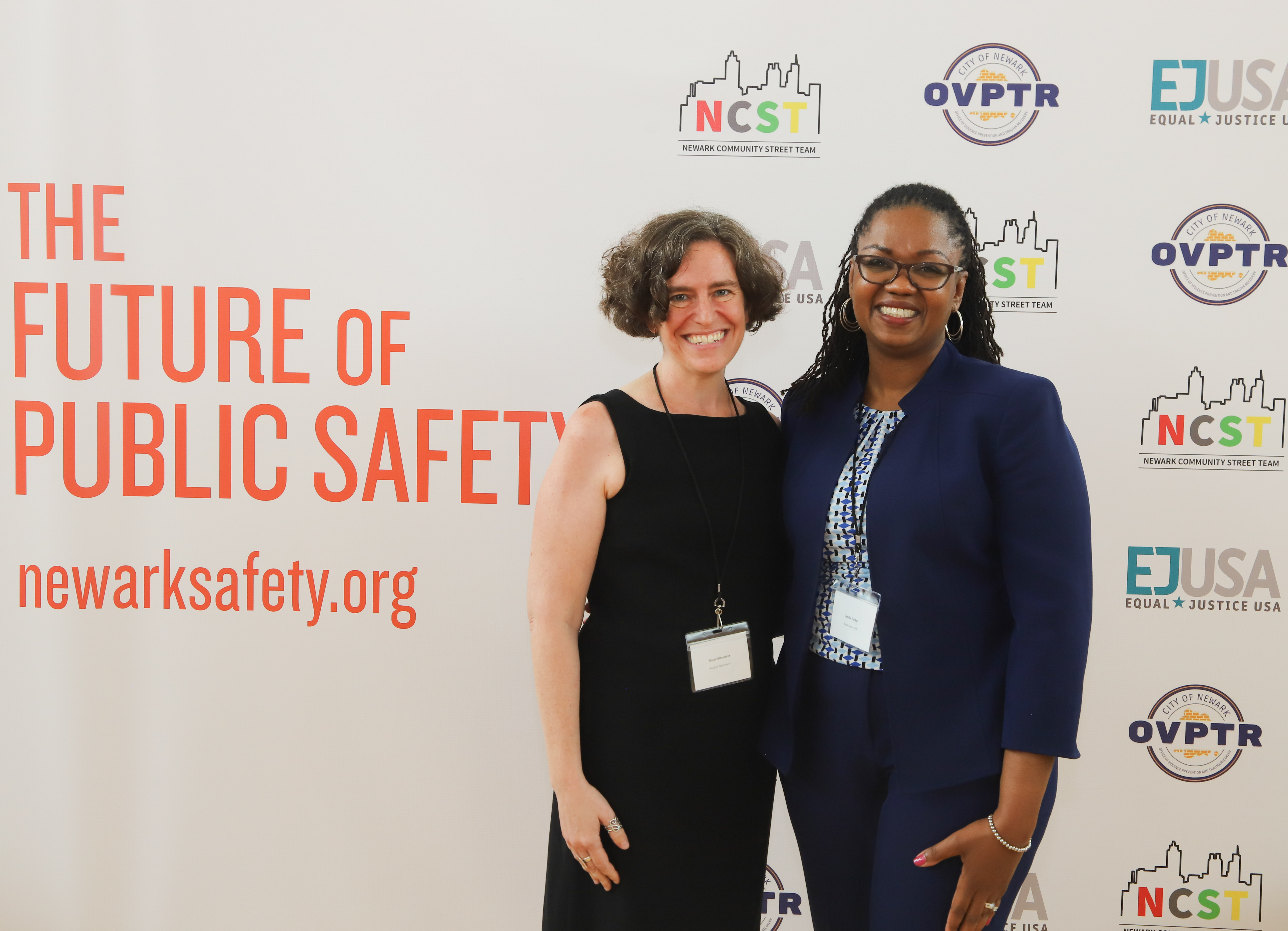 Shari Silberstein and Jamila Hodge pose in front of signage for Newark Safety
