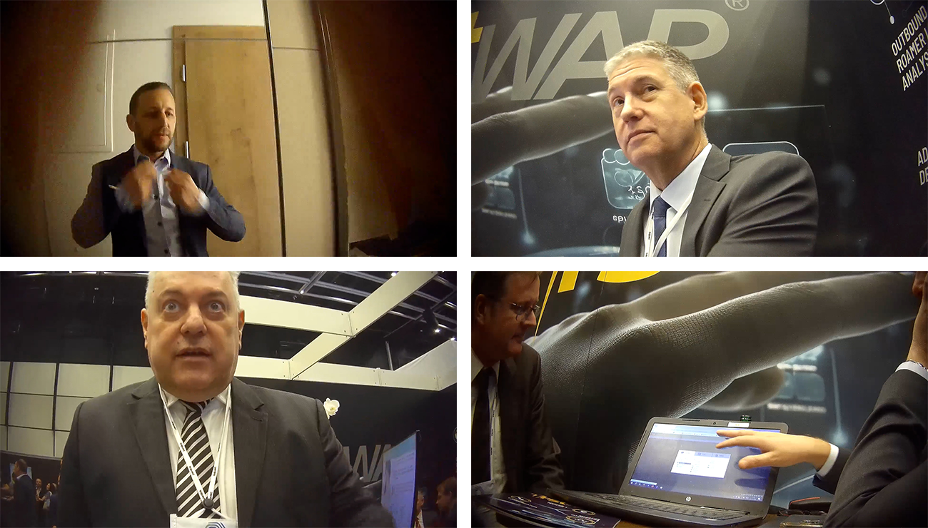 A four-panel grid of video footage showing men in suits at what appears to be a business conference or trade show.

Top left: A man adjusting his tie in front of a wooden door.

Top right: A middle-aged man in a dark suit and tie looking off-camera, with a blurry background featuring the letters "WAP" and a logo.

Bottom left: A middle-aged, balding man in a suit and striped tie looking directly at the camera with a surprised or intense expression.

Bottom right: Two men in suits look at a laptop screen, with one hand pointing to the screen and the other resting on a surface. The background is dark with blurry imagery.