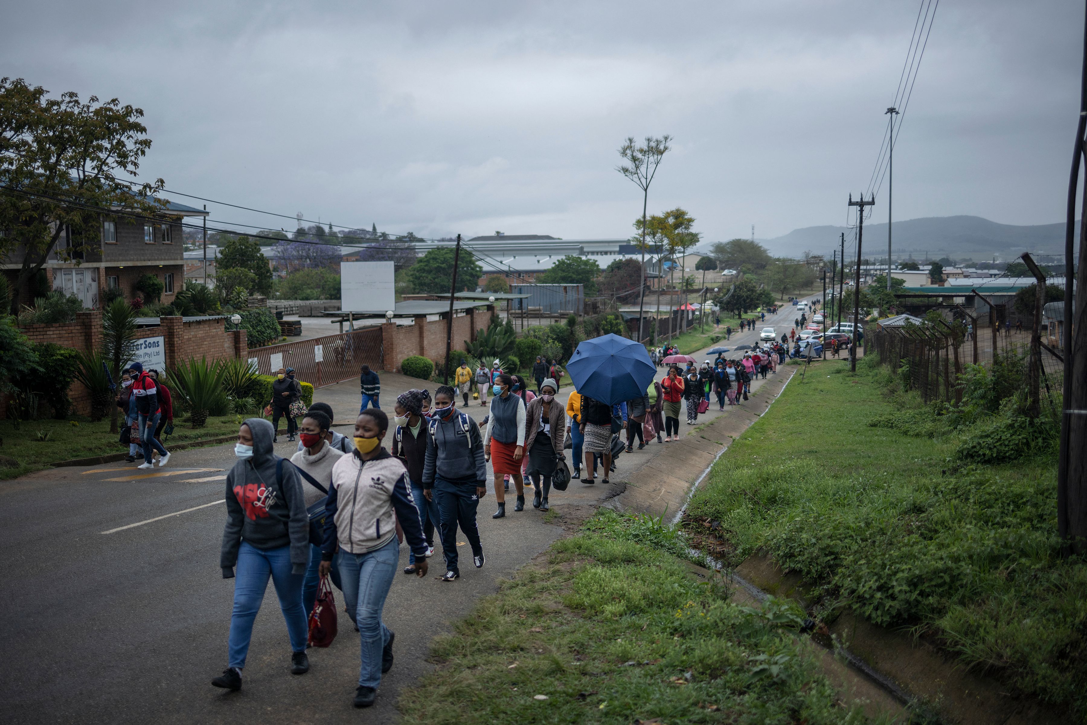 Line of dozens of people walking along the edge of a paved road.