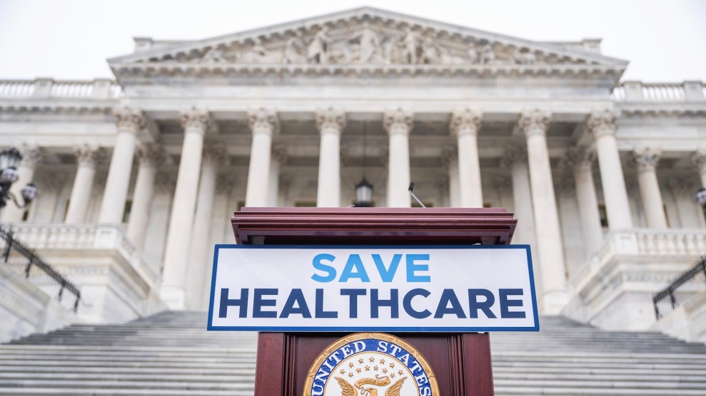 A sign on a podium that says "Save Healthcare" in front of an old building.