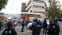 A group of masked police in Border Patrol and DHS uniforms stands outside a building complex