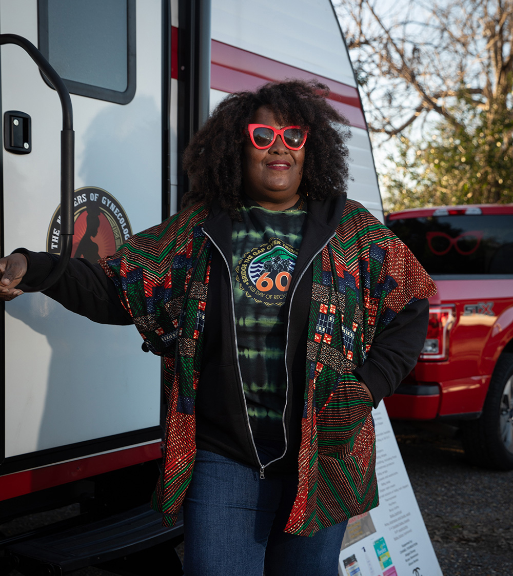 Portrait of African American woman wearing red glasses, standing next to a camping trailer.