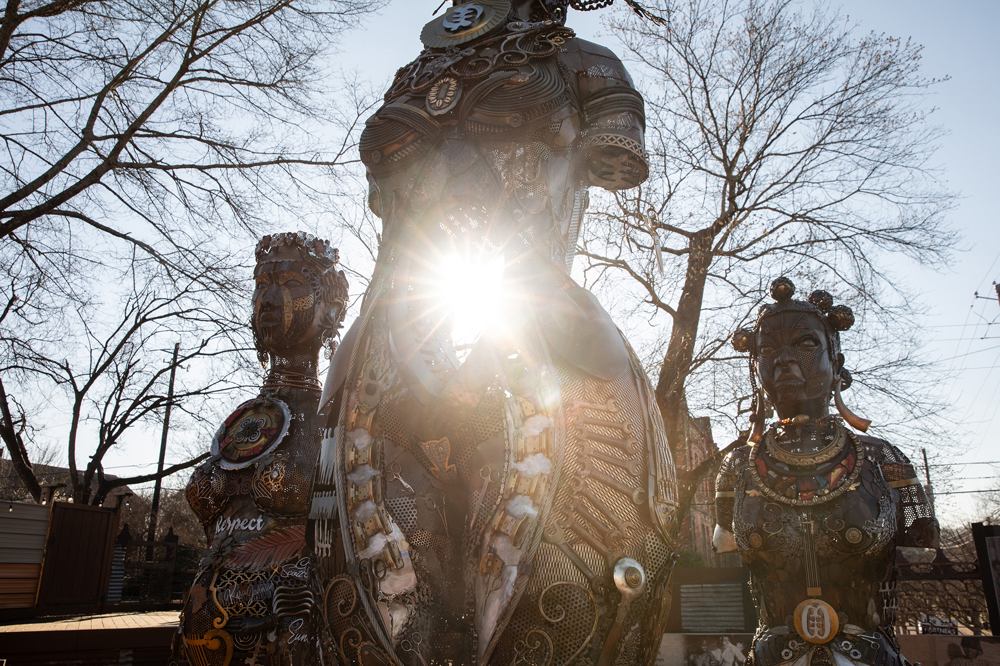 Sun shining through the middle part of a trio of statues of women.