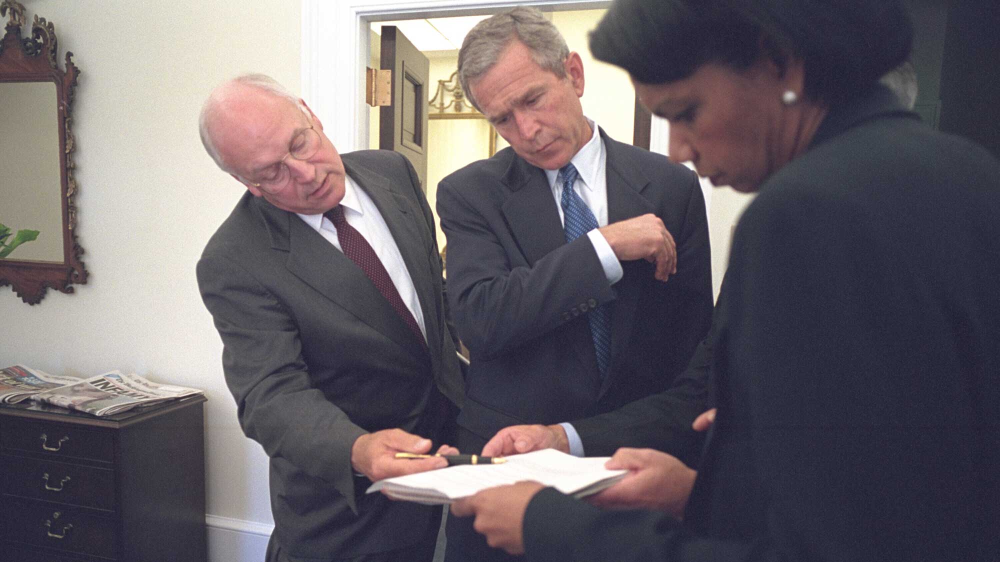 Dick Cheney, George W. Bush and Condoleezza Rice looking over a document.