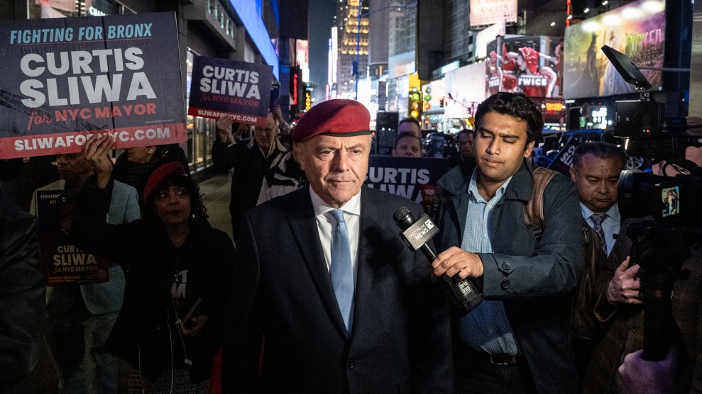 Curtis Sliwa wearing a red beret in Times Square, surrounded by reporters and supporters holding signs.