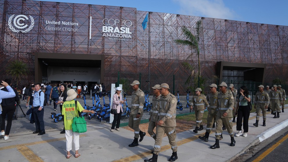 A group of people in grey-green uniforms walk past a building with a sign that says "COP30 BRASIL AMAZONIA"