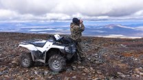 A person next to a white four wheeler looks at the landscape through binoculars.