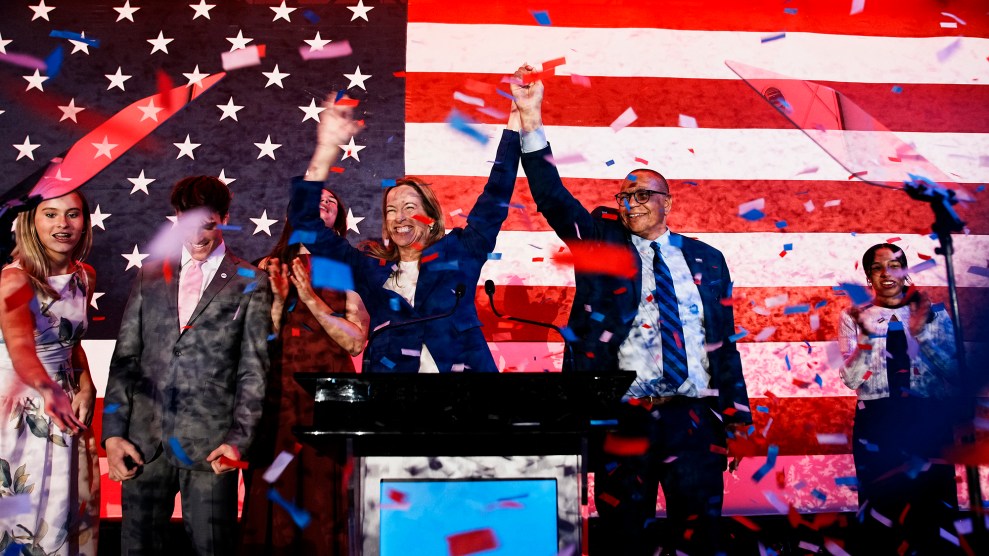 A group of people celebrate under falling red, white, and blue confetti in front of an American flag.